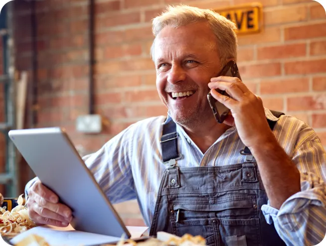 Male Carpenter in Workshop with a Digital Tablet Talking on his Mobile Phone